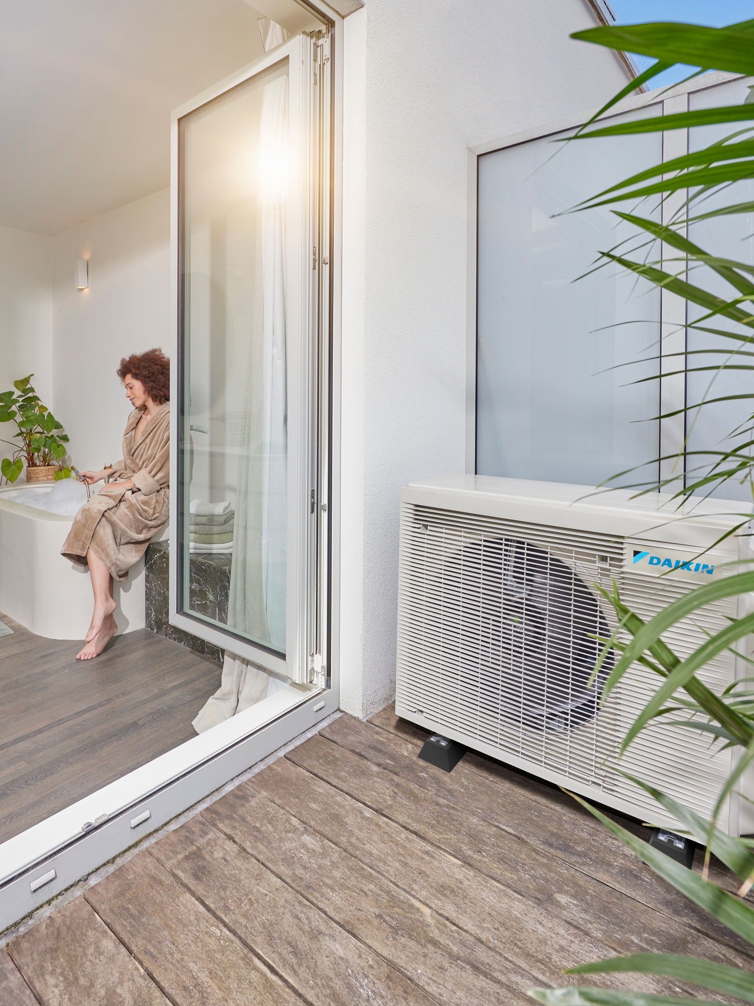 Pompe à chaleur aérothermique installée à côté d'une terrasse avec portes ouvertes sur une salle de bain moderne