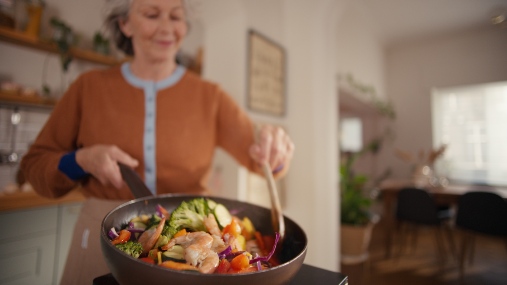 Une femme souriante faisant sauter un sauté de crevettes dans une poêle, générant des odeurs de cuisson