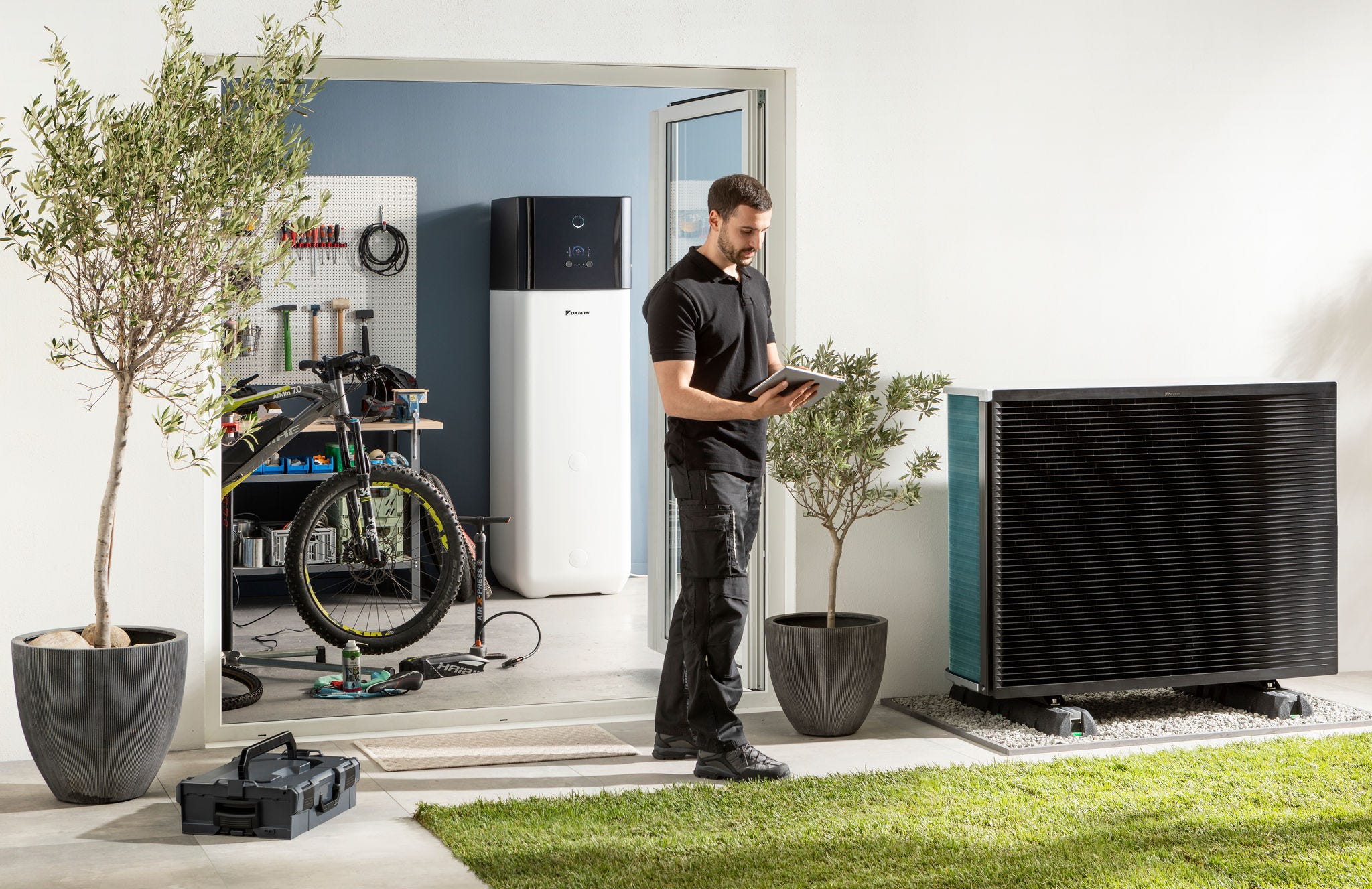 Installateur vérifiant l'unité extérieure d’une pompe à chaleur aérothermique et un ballon d'eau chaude