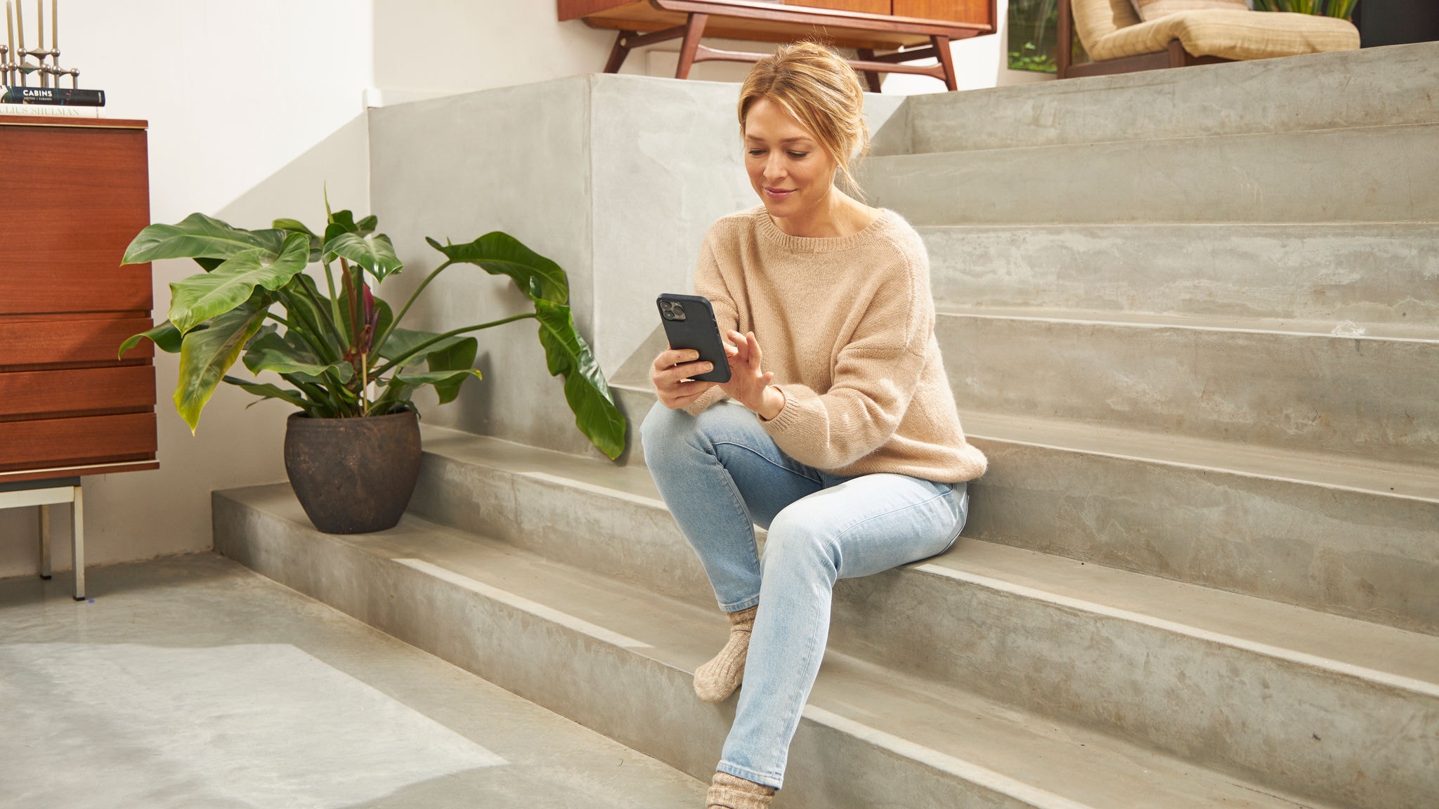 Femme assise sur les escaliers de son logement utilisant l'application Onect sur son téléphone portable