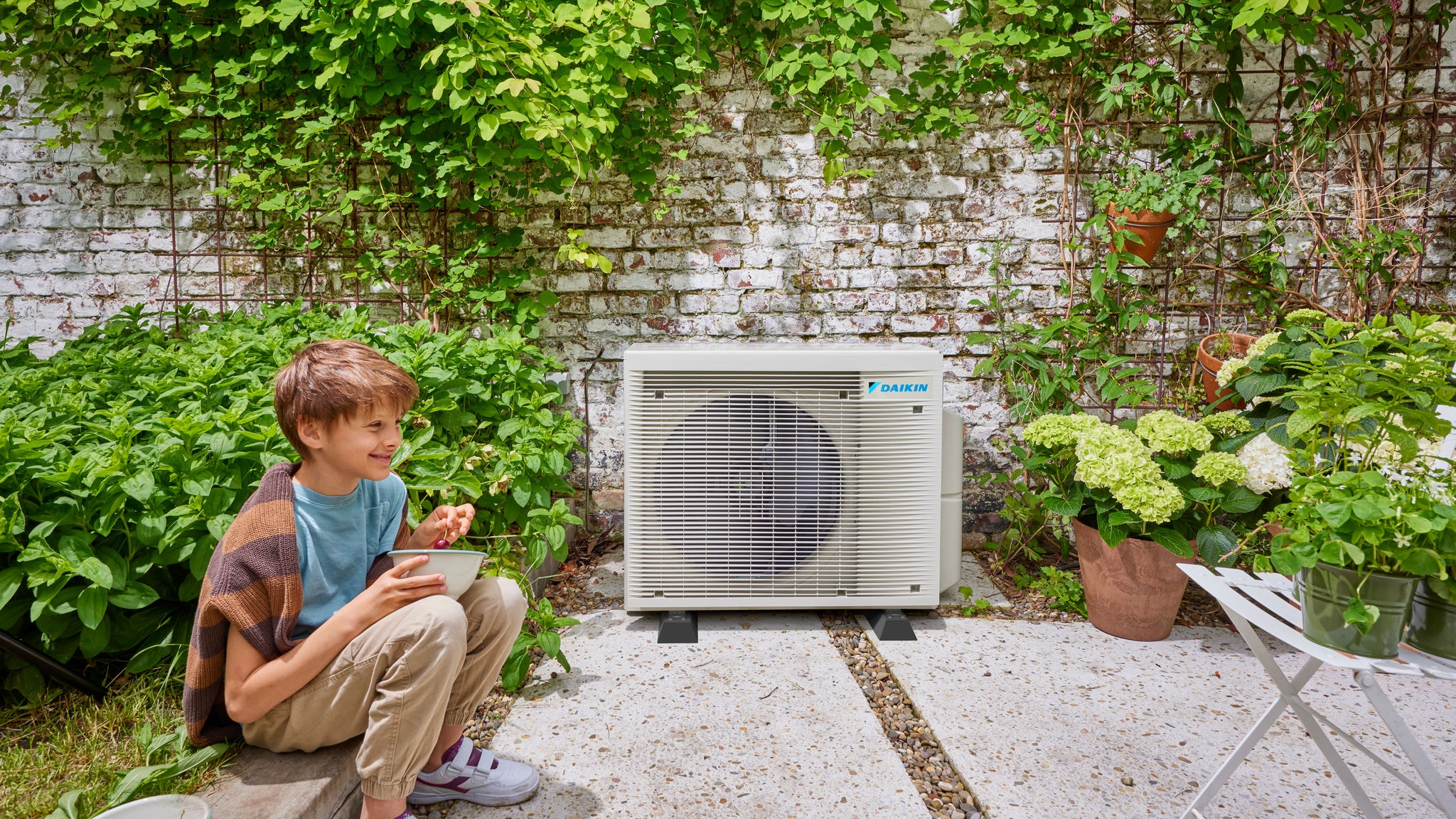 Enfant à proximité d'une unité extérieure pompe à chaleur hybride Daikin, associant l’efficacité énergétique et agréable jardin