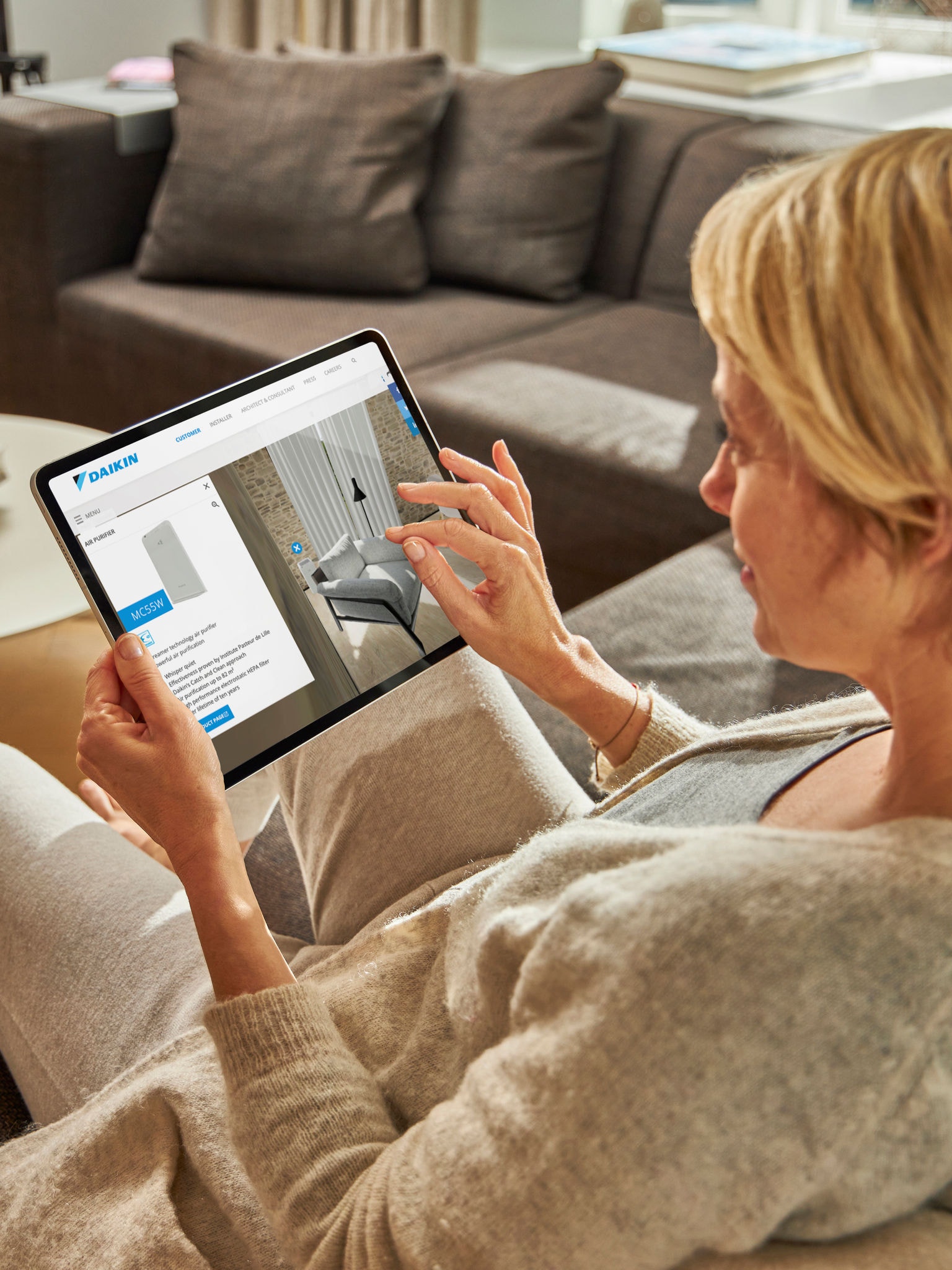 Femme assise sur un canapé regardant sur sa tablette des pompes à chaleur air-eau dans le centre d'expérience virtuelle