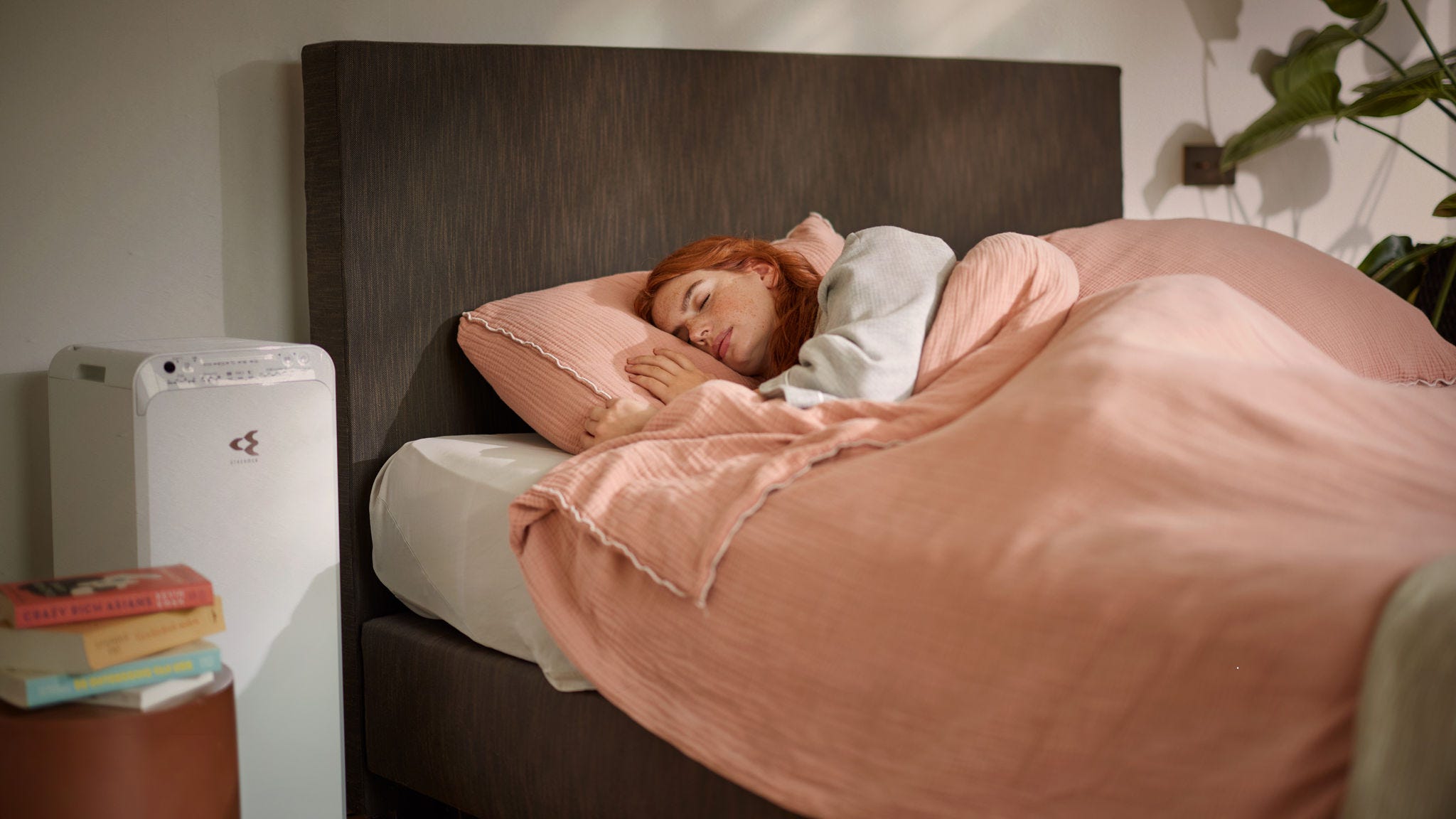 Femme dormant paisiblement dans un lit confortable, avec un purificateur d’air en marche à côté pour assurer une bonne qualité d’air dans la chambre en hiver