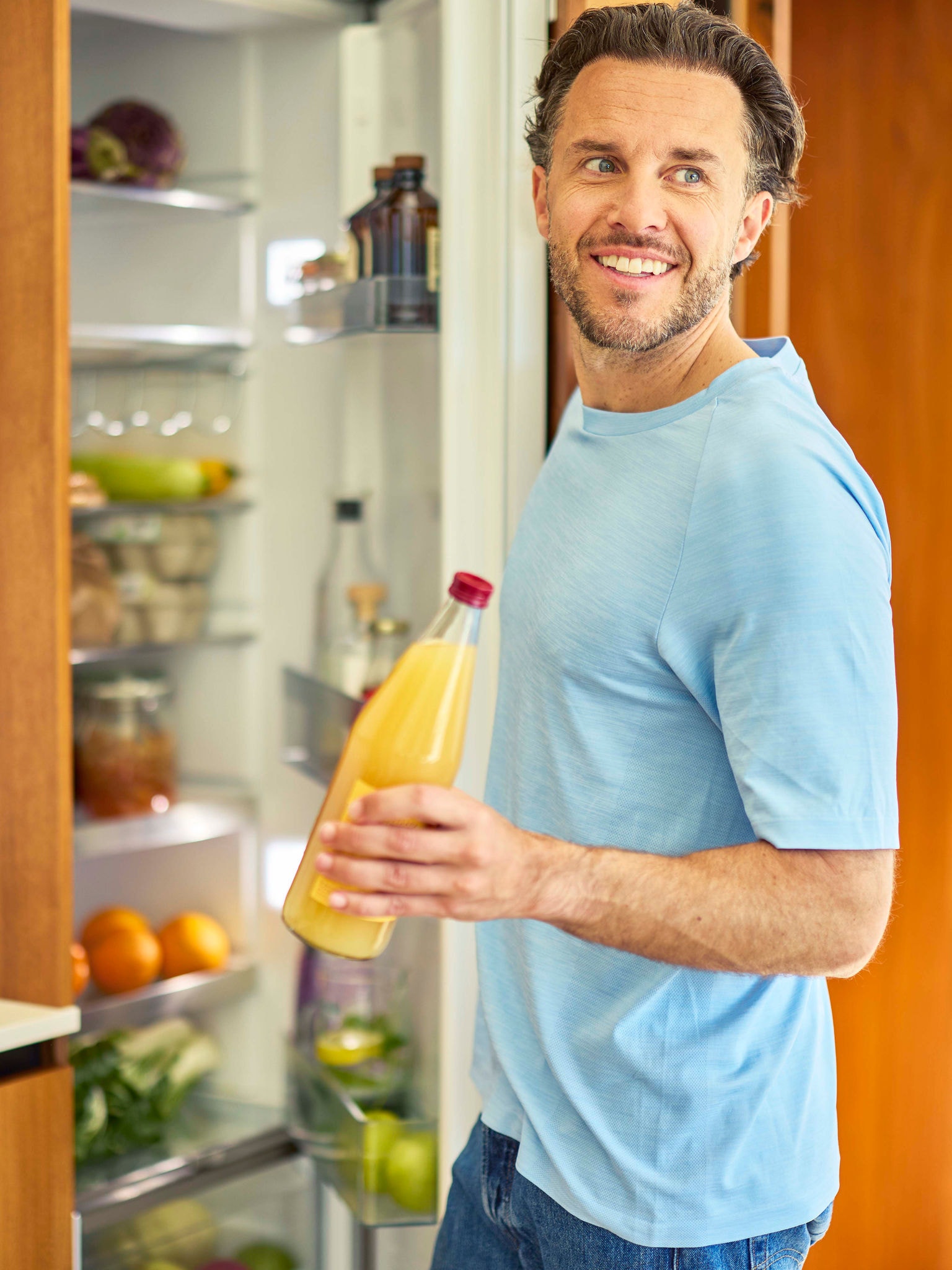 Un homme ouvrant un réfrigérateur et en sortant une bouteille de jus d'orange