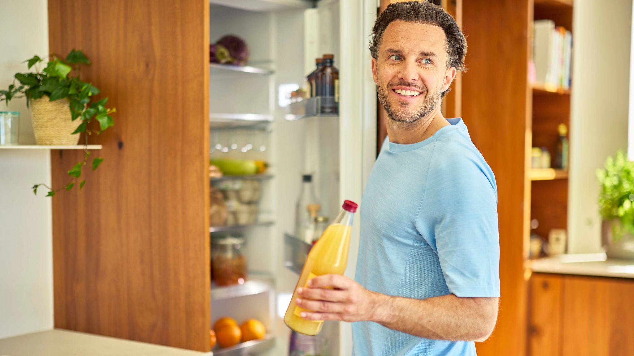 Un homme prenant une bouteille de jus d'orange dans un réfrigérateur dans une cuisine moderne