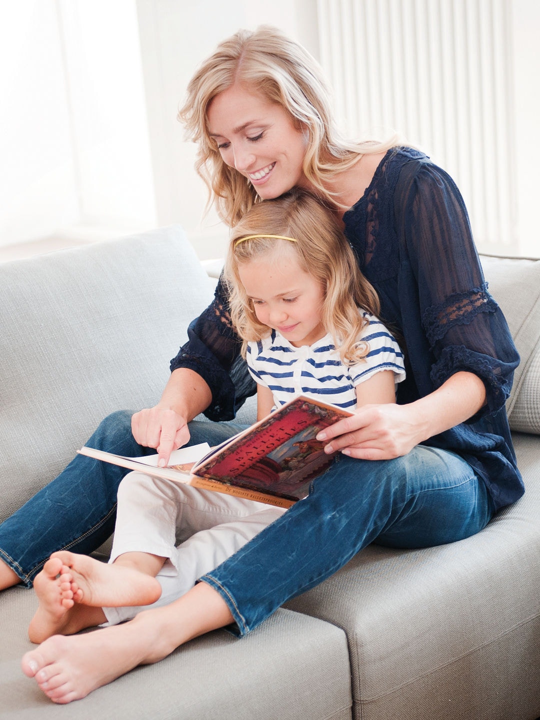 Petite fille assiste sur les genoux de sa mère sur le canapé, les deux lisant un livre ensemble par une température parfaite
