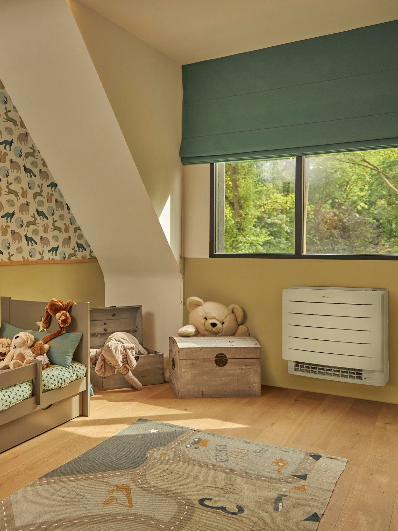 Une chambre d’enfant avec des peluches et un tapis de jeu, avec une pompe à chaleur sur le mur sous une grande fenêtre