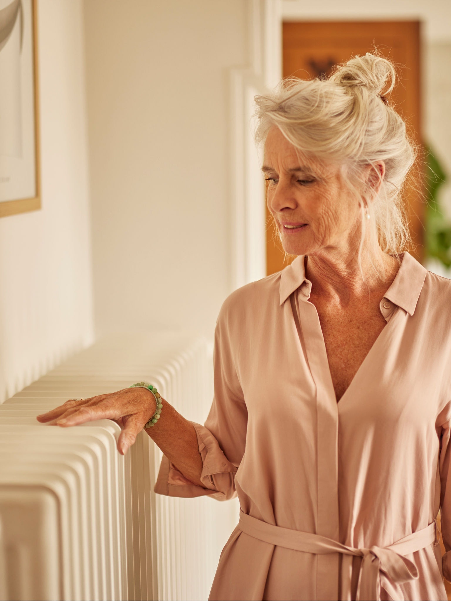 Femme se chauffant les mains sur un radiateur couplé à une pompe à chaleur aérothermique dans une chambre