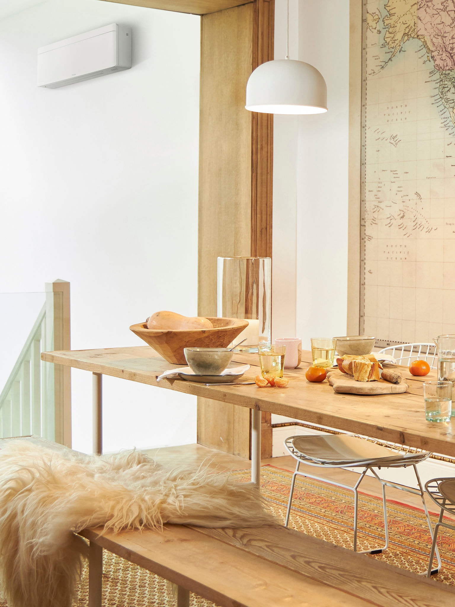 Table de déjeuner dressée avec de la nourriture et des fruits dans une pièce lumineuse, avec un climatiseur visible près de l'escalier.
