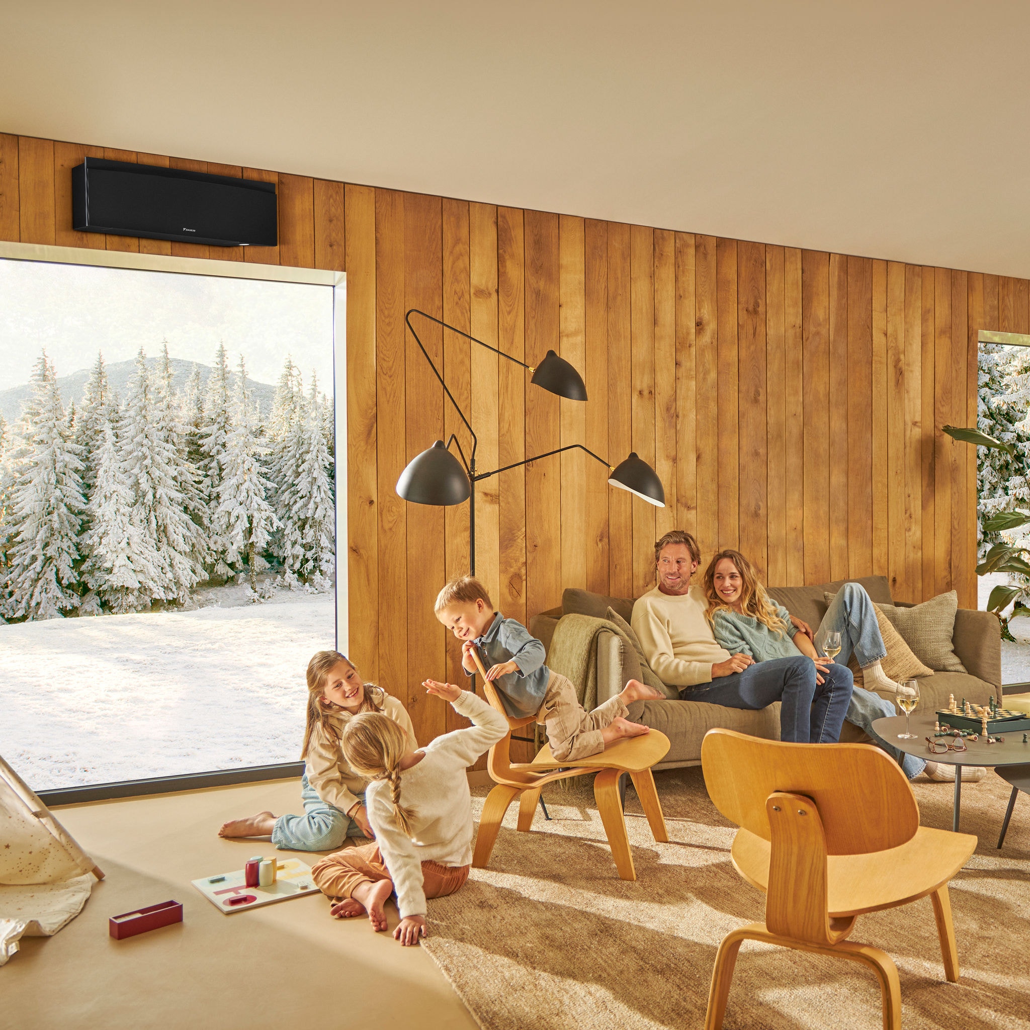 Famille profitant d'un salon chaud et confortable avec un paysage hivernal à l’extérieur, illustrant l’efficacité de nos solutions de chauffage, de rafraîchissement et de ventilation solutions via la création d'un environnement intérieur confortable tout au long de l’année