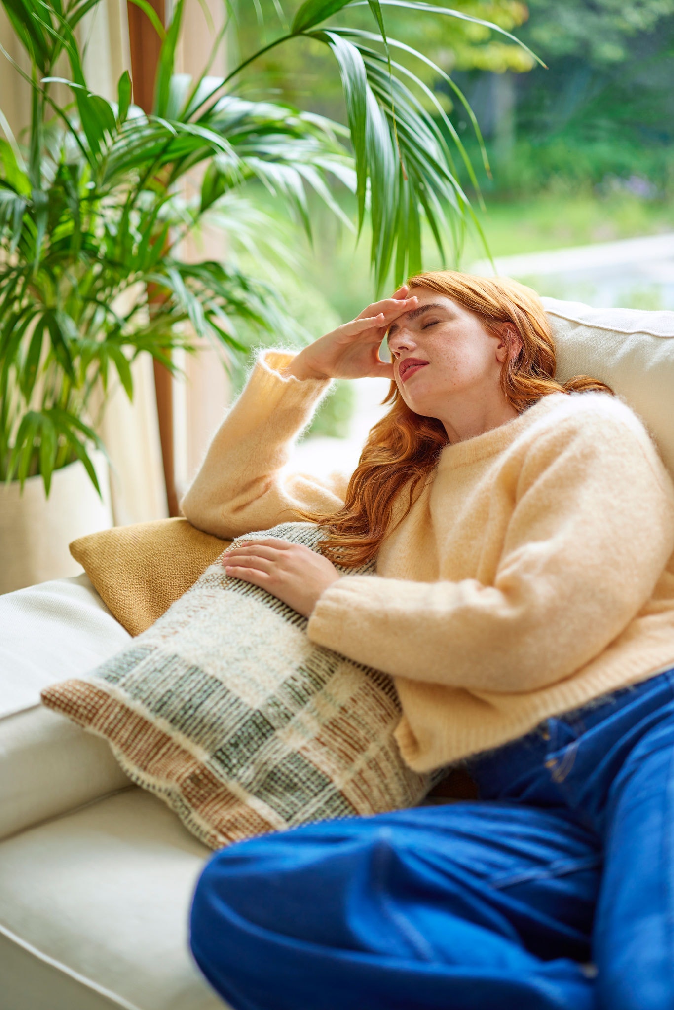 Fille malade sur le canapé souffrant d'un mal de tête, illustrant l'impact d'une mauvaise qualité de l'air et la nécessité de ventilation adéquate