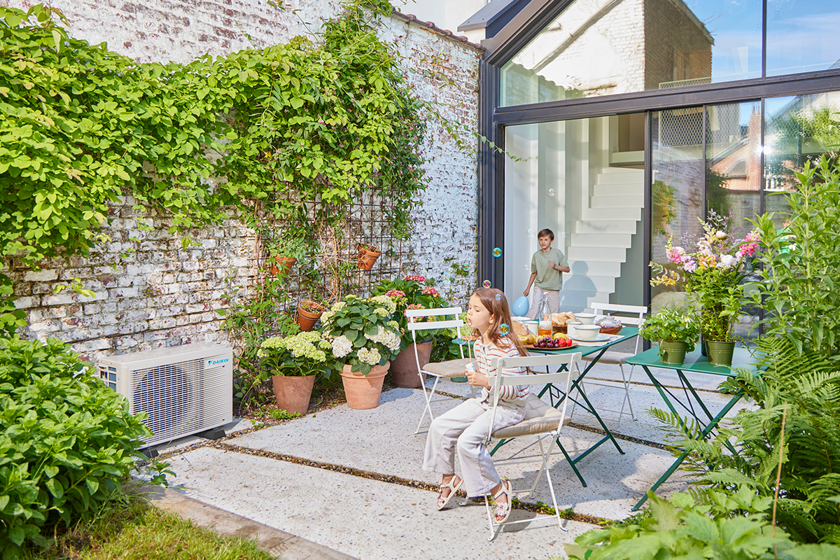 Enfants jouant aux billes sur une terrasse de jardin à côté d'une pompe à chaleur extérieure