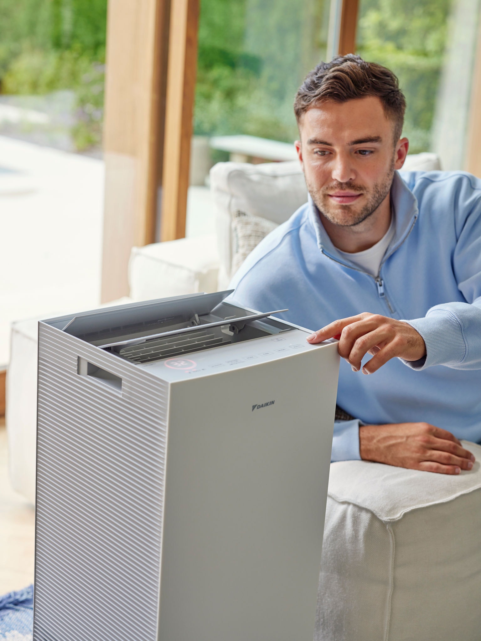Un homme réglant un purificateur d'air Daikin dans un salon pour réduire les allergènes de chat